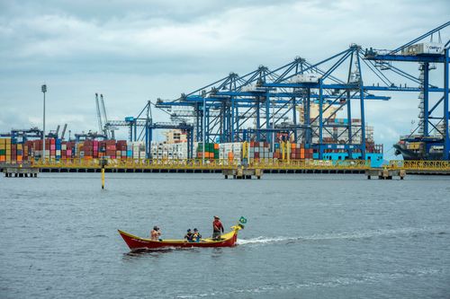 Barco de transporte de passageiros navegando no rio Itiberê e ao fundo Terminal de Contêineres do Porto de P