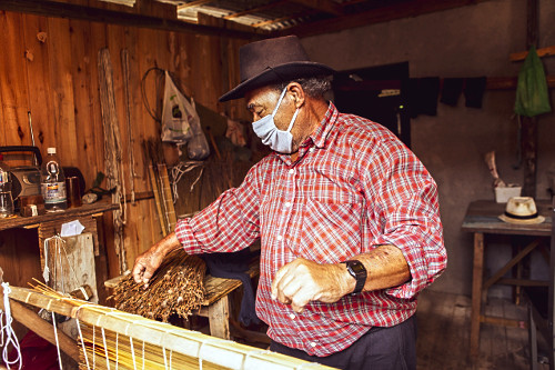 Artesão de comunidade indígena nativa confeccionando esteira em palha de junco para comercialização usando