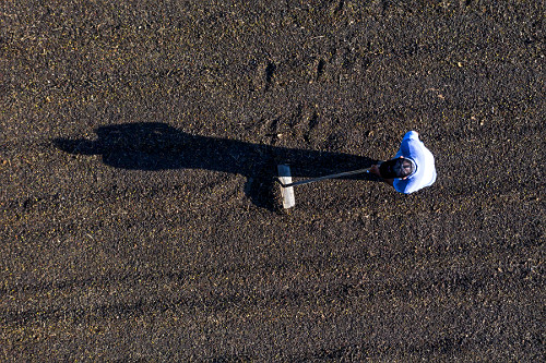 Vista de drone de cafeicultor revirando grãos de café gourmet do tipo catuaí vermelho no terreiro durante s
