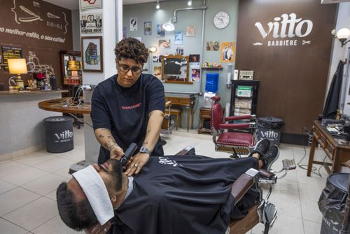 Barbeira fazendo a barba de cliente em barbearia no bairro de Perdizes