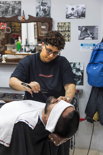 Barbeira fazendo a barba de cliente em barbearia no bairro de Perdizes