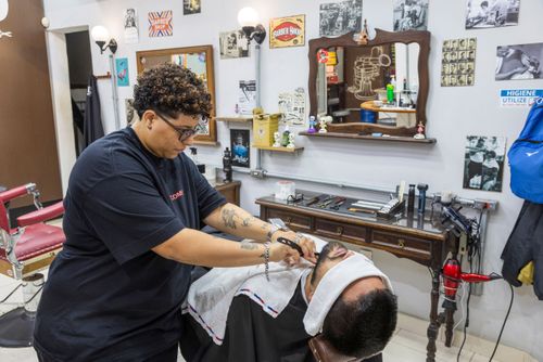 Barbeira fazendo a barba de cliente em barbearia no bairro de Perdizes 