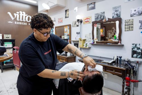 Barbeira fazendo a barba de cliente em barbearia no bairro de Perdizes 