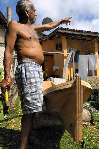 Mestre canoeiro remanescente esculpindo canoa no quintal de sua moradia - Vila de Trindade - 