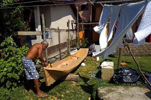 Mestre canoeiro remanescente esculpindo canoa no quintal de sua moradia Vila de Trindade