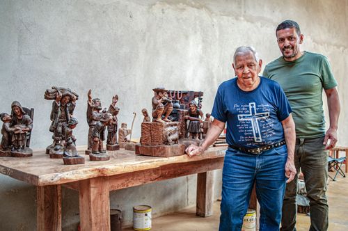 Retrato de artesão e filho posando juntos ao lado de esculturas feitas em madeira