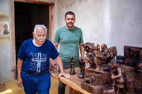 Retrato de artesão e filho posando ao lado de esculturas feitas em madeira