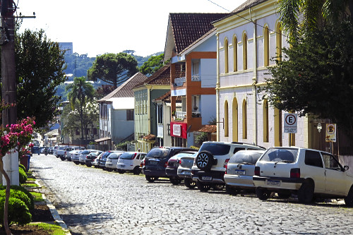 Casas com arquitetura típica italiana e veículos estacionados em rua com declive no centro da cidade - 
