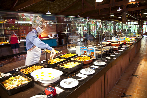 Funcionário usando máscara e protetor facial ao servir buffet em restaurante de hotel-fazenda durante pandem