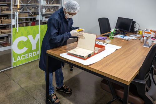 Trabalhadora do Setor de Obras Raras da Biblioteca Pública Estadual Elcy Lacerda fazendo limpeza em livro