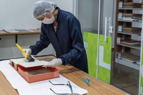 Trabalhadora do Setor de Obras Raras da Biblioteca Pública Estadual Elcy Lacerda fazendo limpeza em livro