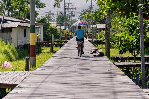 ciclista com sombrinha para se proteger do sol na passarela de madeira de acesso às casas flutuantes em área
