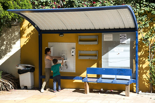 Mãe e filho utilizando serviços disponíveis em ponto de ônibus - água filtrada