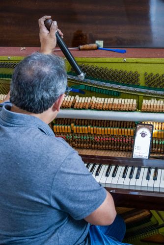 Profissional afinando piano de parede usando afinador digital no telefone celular