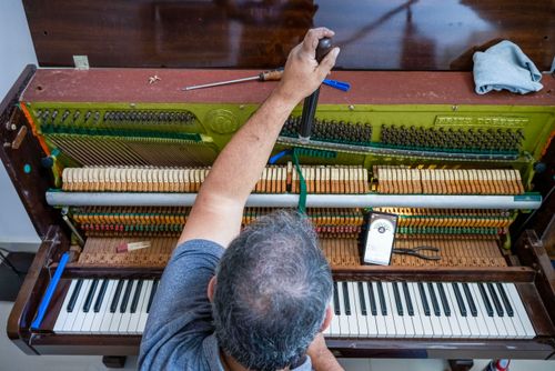 Profissional afinando piano de parede usando afinador digital no telefone celular