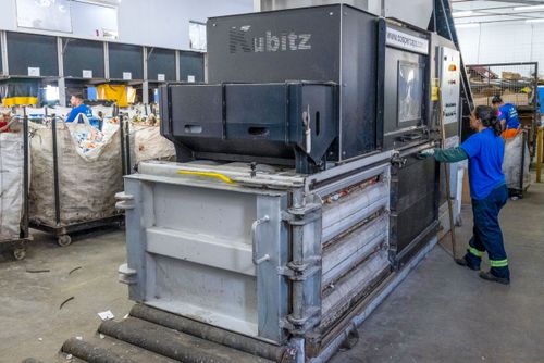 Cooperada acionando prensa enfardadeira para compactação de material reciclável em cooperativa de catadores