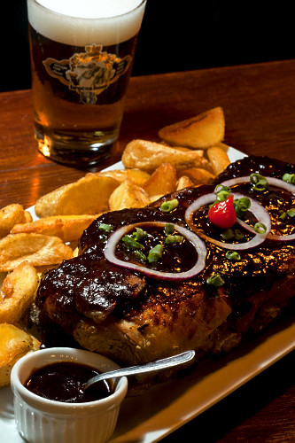 Costelinha de porco com batatas e copo de chope ao fundo servido em restaurante