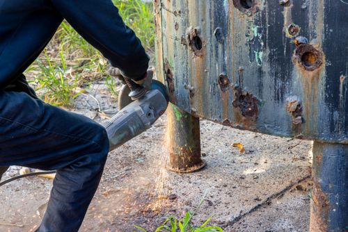 Serralheiro cortando chapa metálica de caldeira industrial com esmerilhadeira
