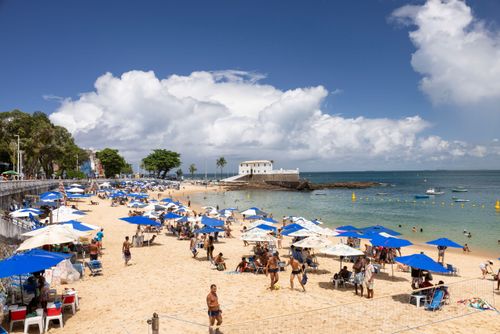 Vista de cima de banhistas e guarda-sóis na Praia do Porto da Barra - Forte de Santa Maria ao fundo