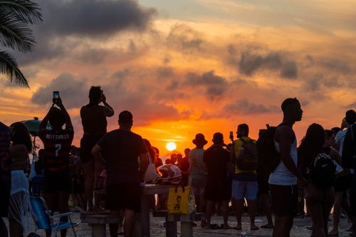 Pessoas apreciando o pôr do sol na Praia do Arpoador