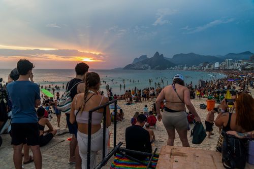 Pessoas apreciando o pôr do sol na praia do Arpoador