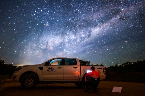 Integrante da ONG Xingu+Catu conectado a internet no Parque Indígena do Xingu sob céu estrelado e via lácte