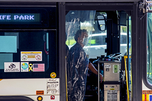 Detalhe de motorista de ônibus protegido por cortina de plástico e máscara durante pandemia do coronavírus