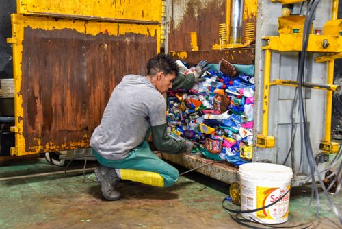Trabalhador utilizando prensa hidráulica em cooperativa de separação de recicláveis