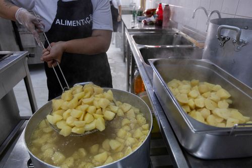 Cozinheira retirando batata cozida de panela em restaurante de preço popular 