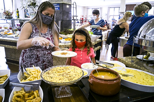 Mãe e filha se servindo em buffet de restaurante com máscaras e luvas descartáveis para se proteger do COVI