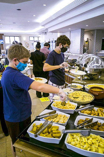 Irmãos se servindo em buffet de restaurante com máscaras e luvas descartáveis para se proteger do COVID-19 